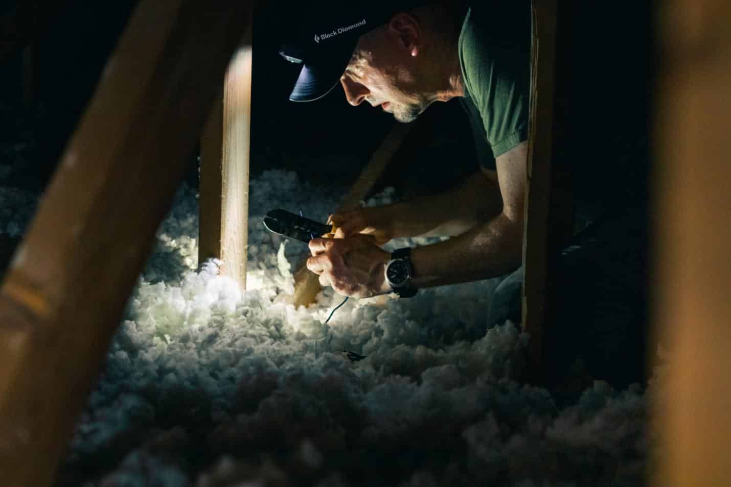 Person examining attic insulation with a flashlight.