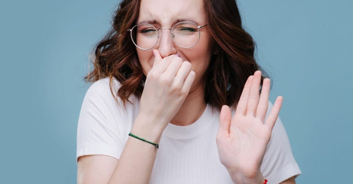 A young woman holds her nose against a bad smell, wondering how to remove odor from air ducts