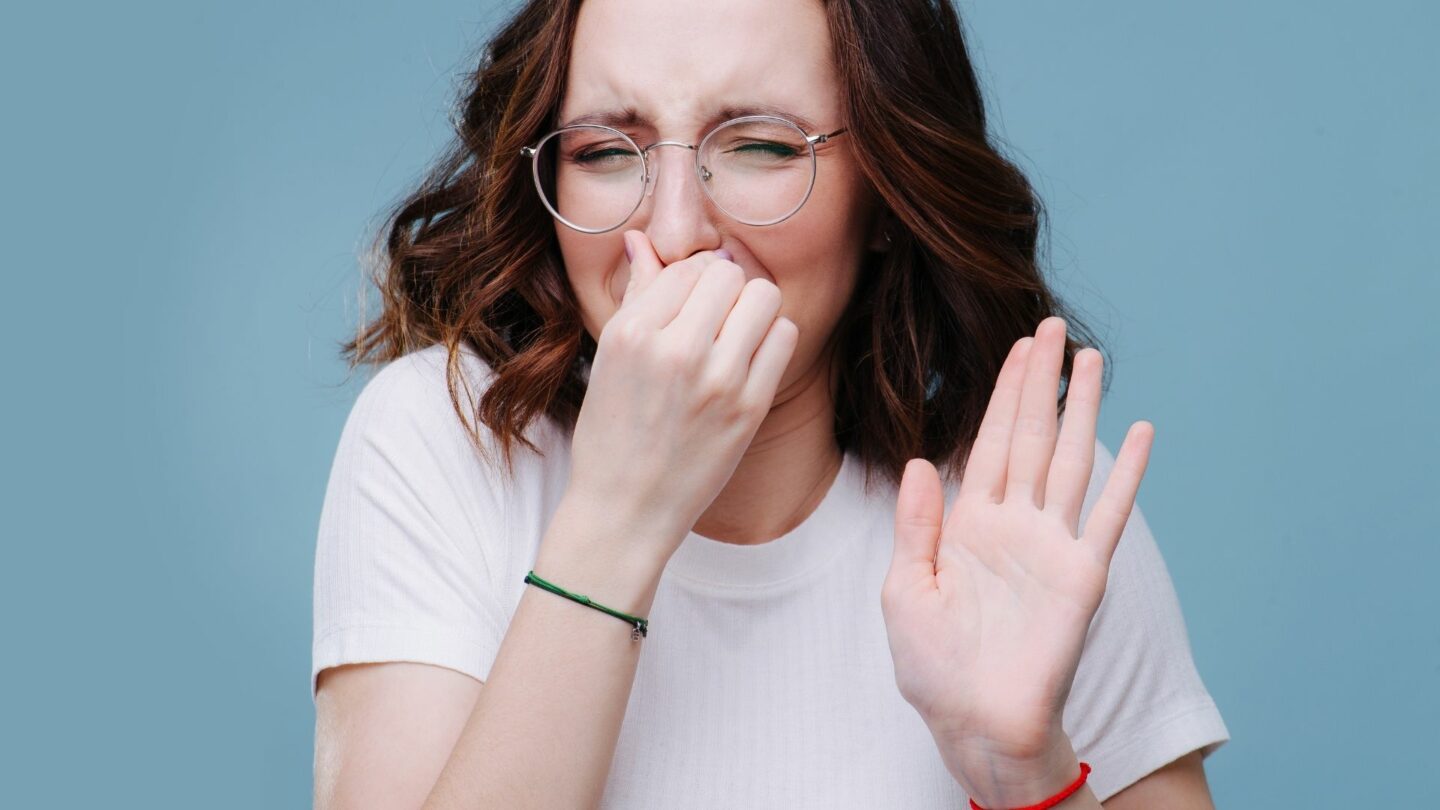 A young woman holds her nose against a bad smell, wondering how to remove odor from air ducts