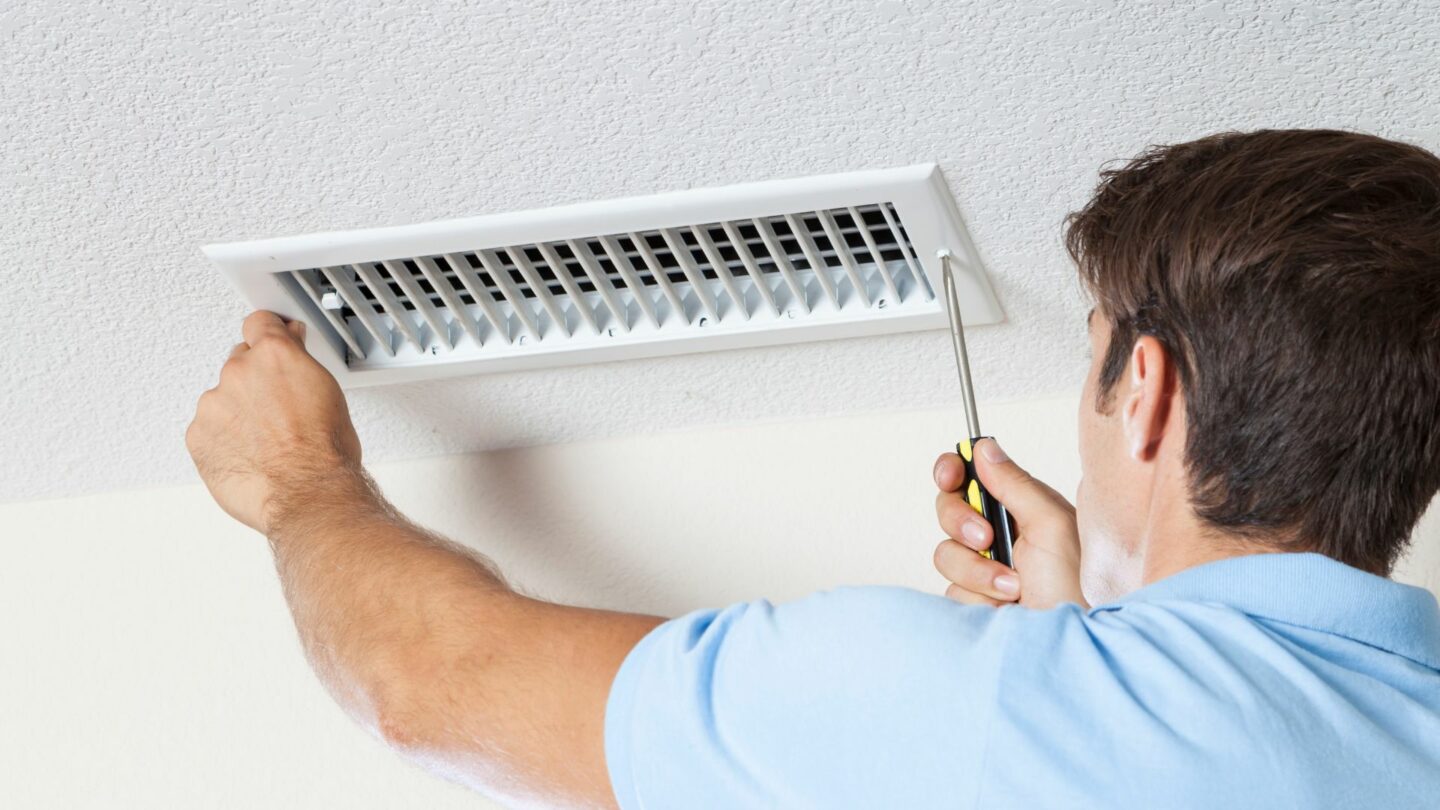 A worker unscrews an air vent to perform air duct repair