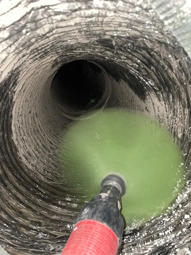 Close-up of air duct interior being cleaned with rotating brush tool removing dust and debris.
