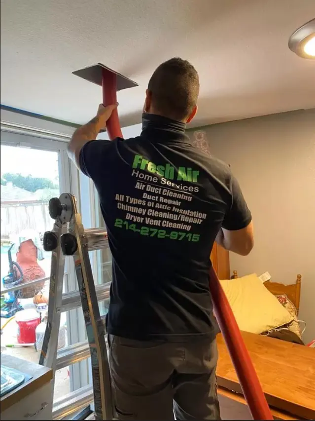 Technician from Fresh Air Home Services cleaning an air duct in a residential ceiling using a red hose.