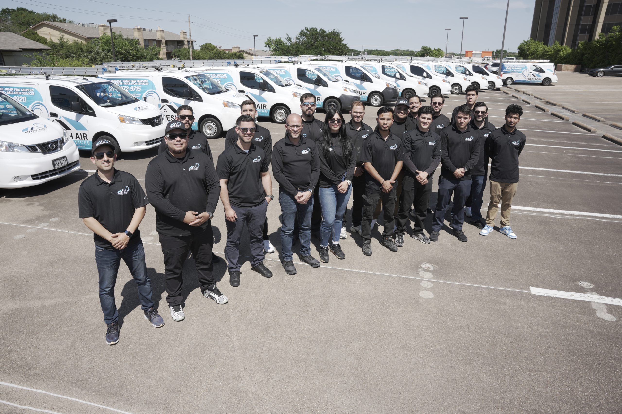 Fresh Air Home Services team standing together in front of branded HVAC vans lined up in a parking lot.