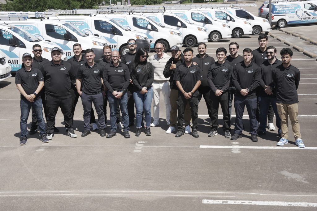HVAC company team posing together in front of a fleet of Fresh Air Home Services vans in a parking lot.