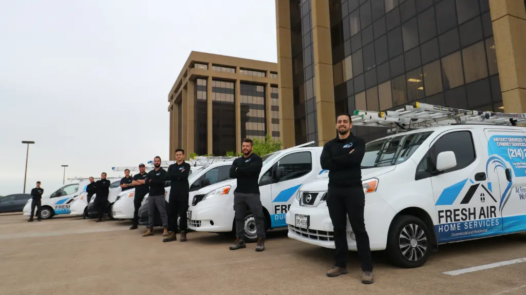 HVAC team standing confidently beside Fresh Air Home Services vans in front of office buildings.
