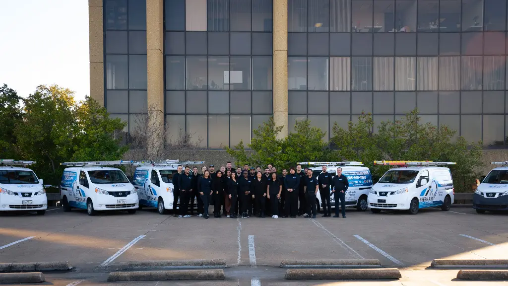 HVAC service team standing in front of company vans with branded graphics outside an office building.