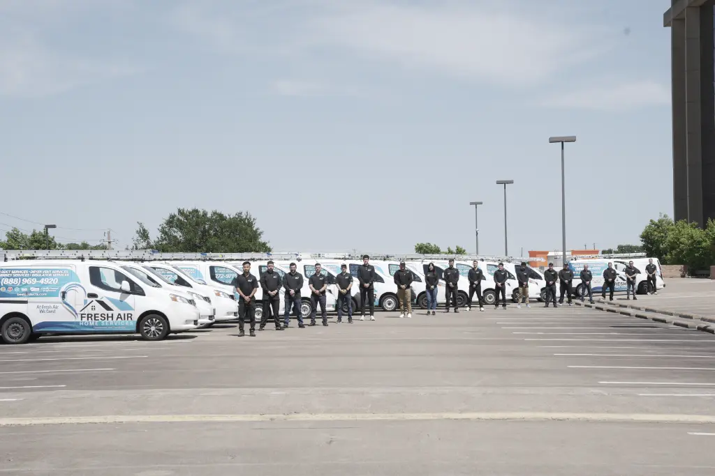HVAC technicians standing beside a long row of branded service vans in a large parking lot under clear skies.