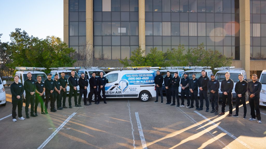 HVAC technicians lined up in front of branded service vans in a parking lot outside an office building.