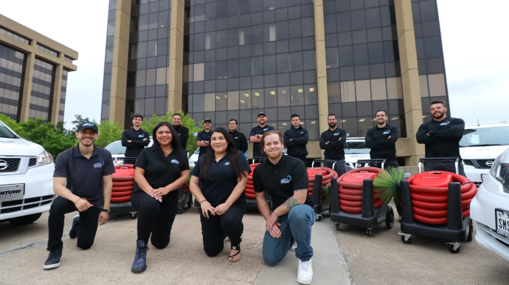 Team of air duct cleaning professionals posing in front of commercial building with service vans and cleaning equipment.