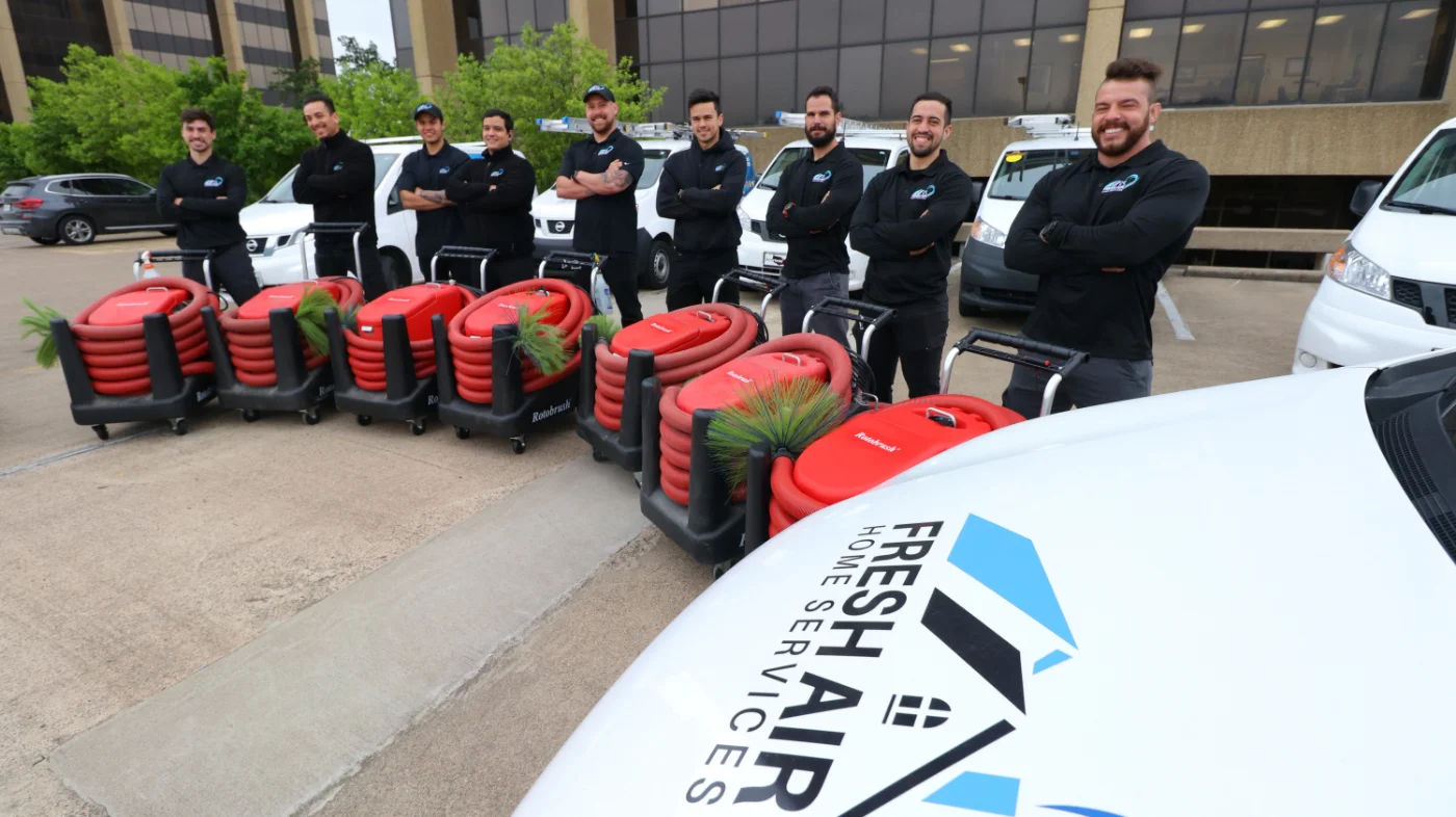 Air duct cleaning team from Fresh Air Home Services standing beside red cleaning equipment and service vans.